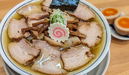 A bowl of rich ramen topped with slices of chashu pork, narutomaki, and seasoned eggs.