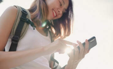 A cheerful traveler using her smartphone outdoors, capturing moments and staying connected during her journey