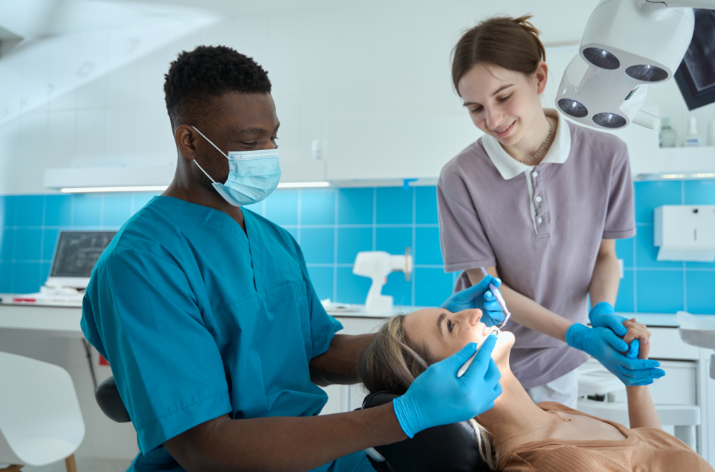 A dentist and dental assistant providing general dental services to a patient in a modern dental clinic, with the dentist focused on examining the patient’s teeth and the assistant offering support.