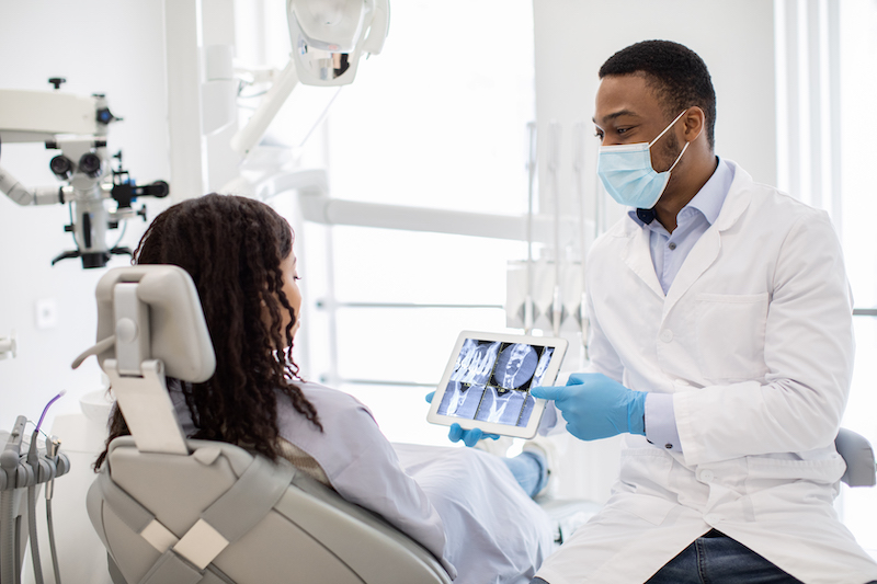 Male dentist showing a female patient her dental X-rays on a digital tablet. Understanding how long does a dental check up take can ease anxiety and provide a clear picture of oral health.