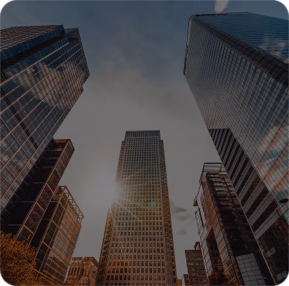 Sun shining between tall modern skyscrapers in a city under a blue sky.