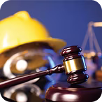 Judge's gavel in focus with a blurred yellow construction helmet and legal scales in the background.