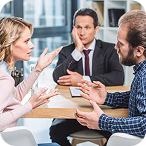 Three professionals engaged in a serious discussion around a table in an office setting.