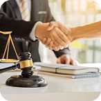 Two people shaking hands over a desk with a judge's gavel and scales of justice.