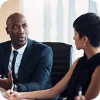 Two professionals in business attire engaged in a discussion in an office setting.