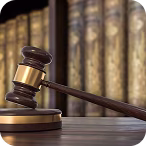 Wooden judge's gavel resting on a sound block with blurred law books in the background.