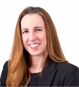 Smiling woman with long light brown hair wearing a black blazer and black top against a white background.