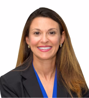 Woman with long brown hair wearing a black blazer and blue blouse, smiling against a light gray background.