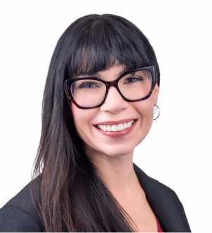 Smiling woman with straight brown hair, glasses, and bangs wearing a black blazer against a dark background.