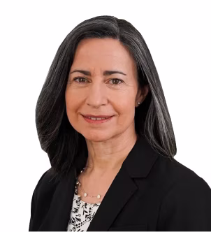 Professional woman with shoulder-length dark hair and gray streaks, wearing a black blazer and patterned blouse, smiling against a white background.