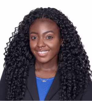 Smiling woman with long black hair wearing a dark blazer in front of a brick wall.