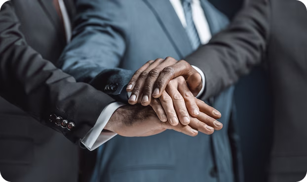 Three diverse people in business suits stacking their hands in a team gesture.