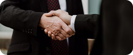 Two men shaking hands in a modern office with two colleagues watching and smiling.