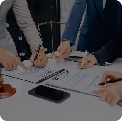 Four people in business attire reviewing and signing documents on a table with a scale of justice and a smartphone nearby.