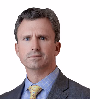 Professional headshot of a man with short brown hair wearing a dark suit, white shirt, and red patterned tie.