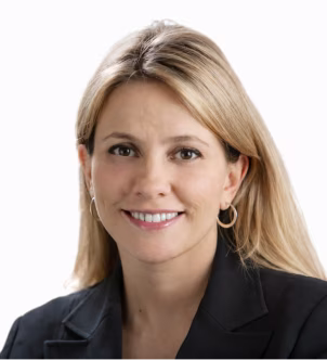 Smiling woman with blonde hair wearing a black blazer and hoop earrings against a white background.