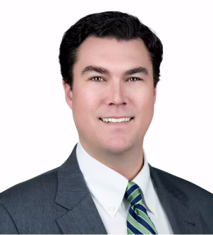 Smiling woman with long dark hair wearing a black blazer and pearl necklace on a white background.