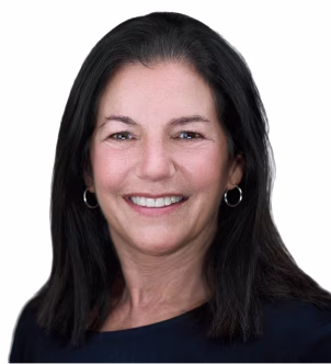 Smiling woman with long brown hair wearing a black blazer and pearl earrings against a white background.