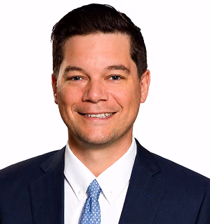 Smiling man in a dark suit, white shirt, and striped tie against a white background.
