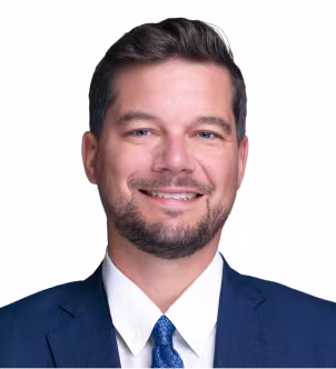 Smiling man in a dark suit, white shirt, and striped tie against a white background.