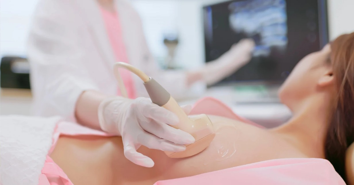 Breast ultrasound being performed on young woman by sonographer