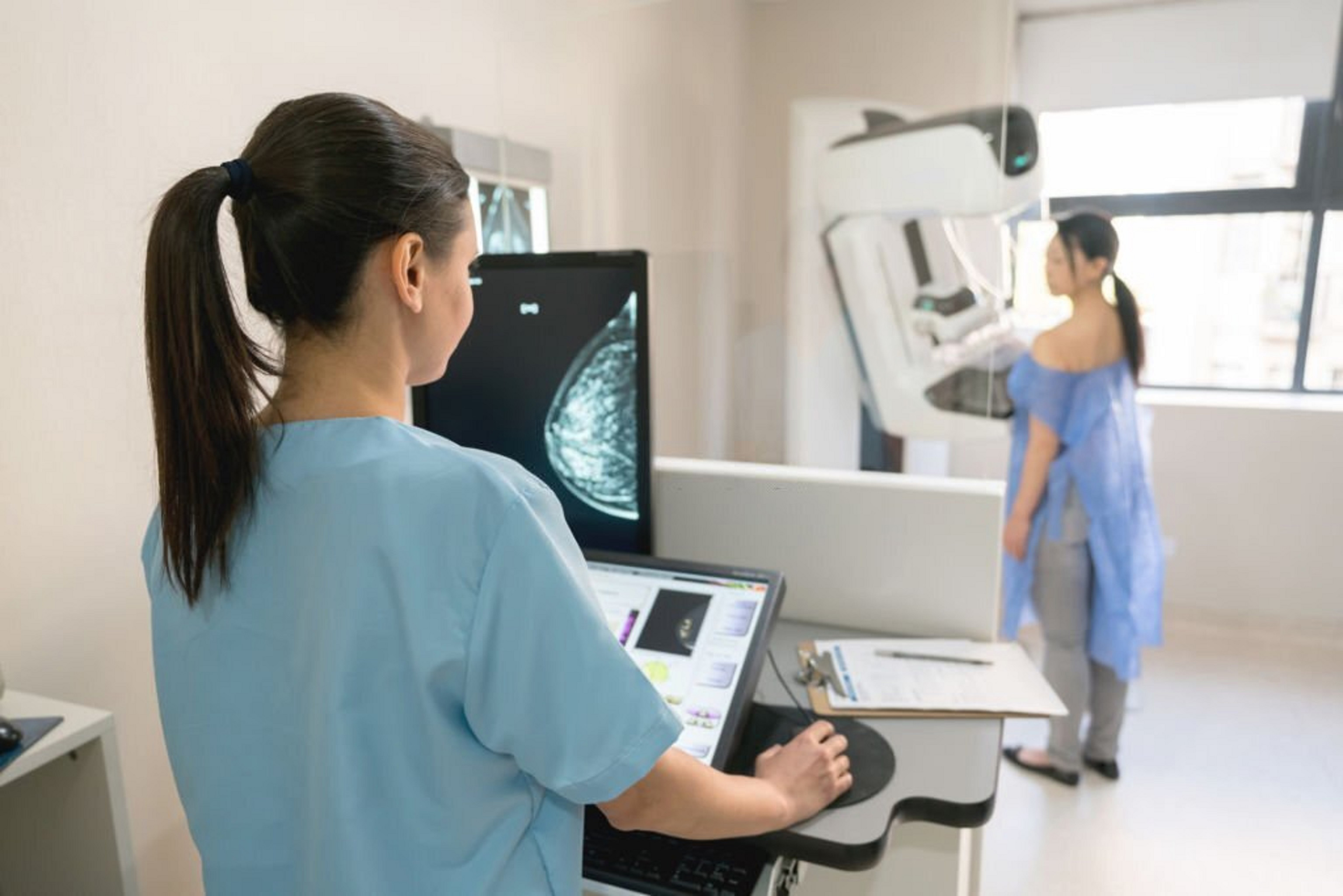Mammogram scan displayed on a screen during breast imaging review with young woman in background near a mammogram machine