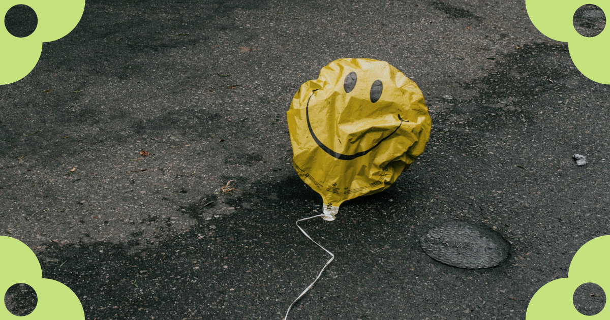 A deflated balloon with a happy face lying on cracked asphalt.s