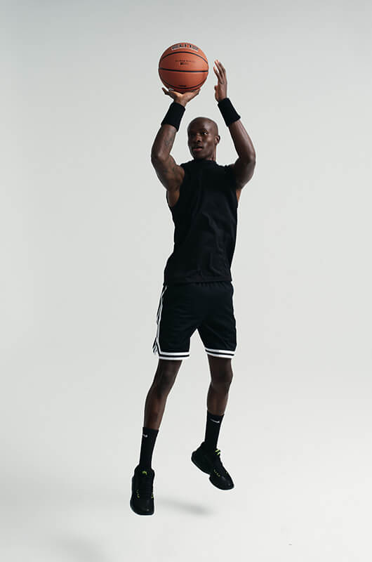 Male basketball player in black athletic wear jumping and preparing to shoot a basketball against a plain light background.