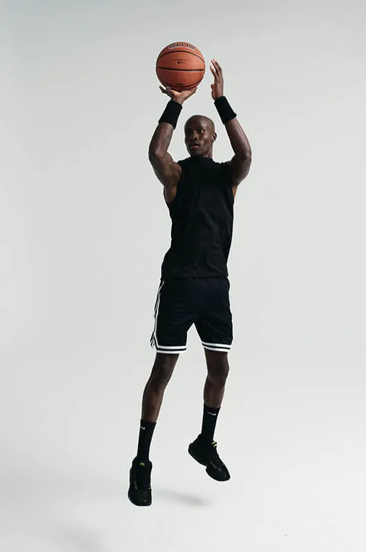 Male basketball player in black athletic wear jumping and preparing to shoot a basketball against a plain light background.