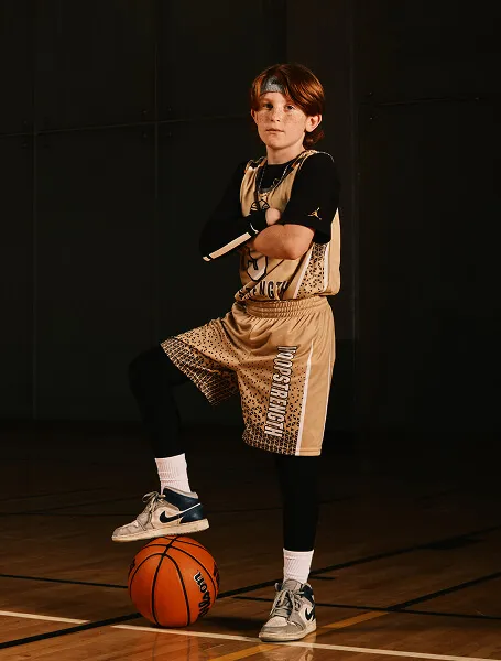 HoopStrength youth basketball athlete posing confidently during a Media&Motion Calgary sports media day, with one foot resting on the ball.