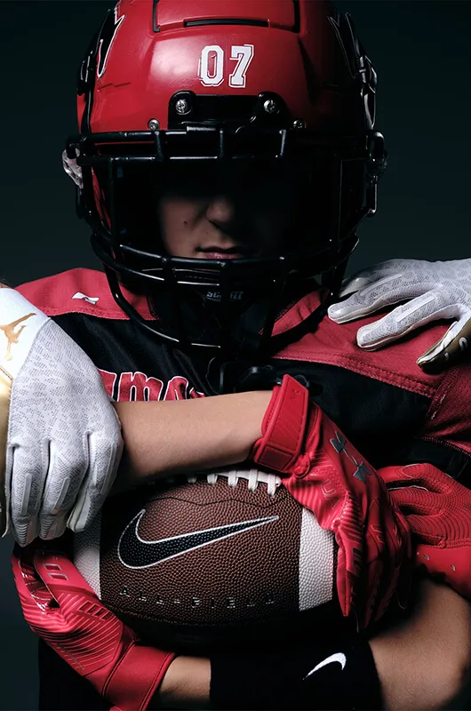 American football player wearing a red helmet with number 07, holding a Nike football tightly with gloved hands.