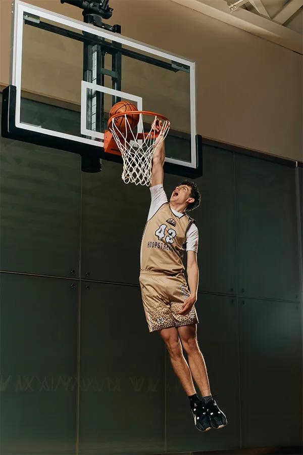 Young basketball player in beige uniform jumping to dunk the ball into the hoop indoors.
