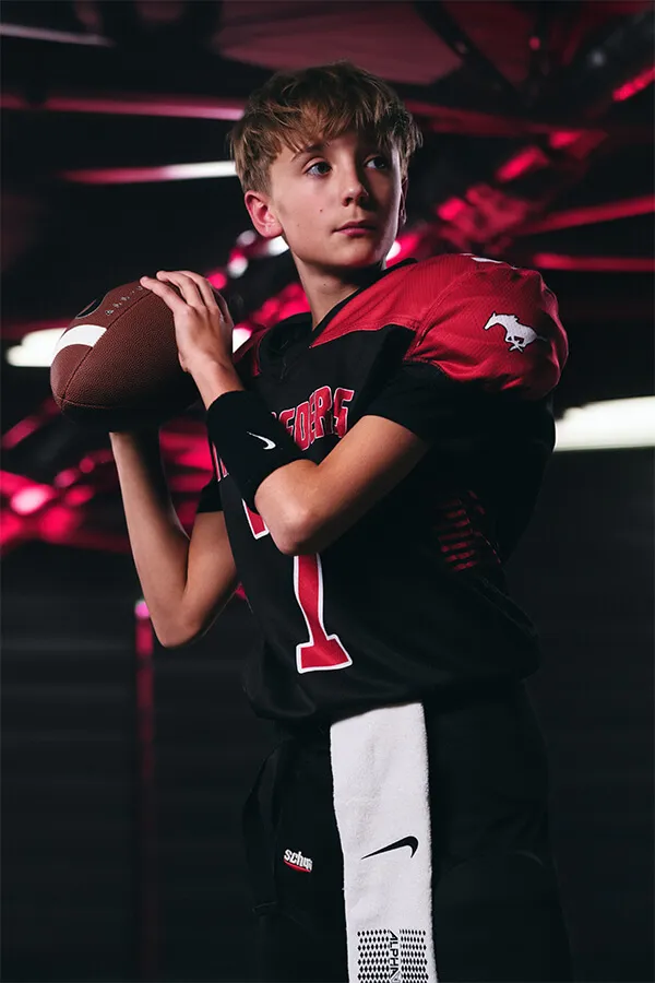 Young football player in black and red uniform holding a football ready to throw.