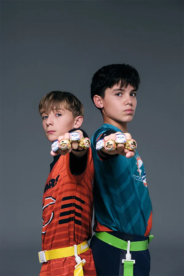 Two boys standing back-to-back, each extending a fist wearing multiple championship rings.
