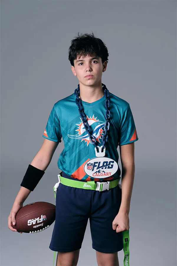 Young boy wearing a teal Miami Dolphins NFL flag football jersey holding a football with NFL Flag Calgary belt and flags.