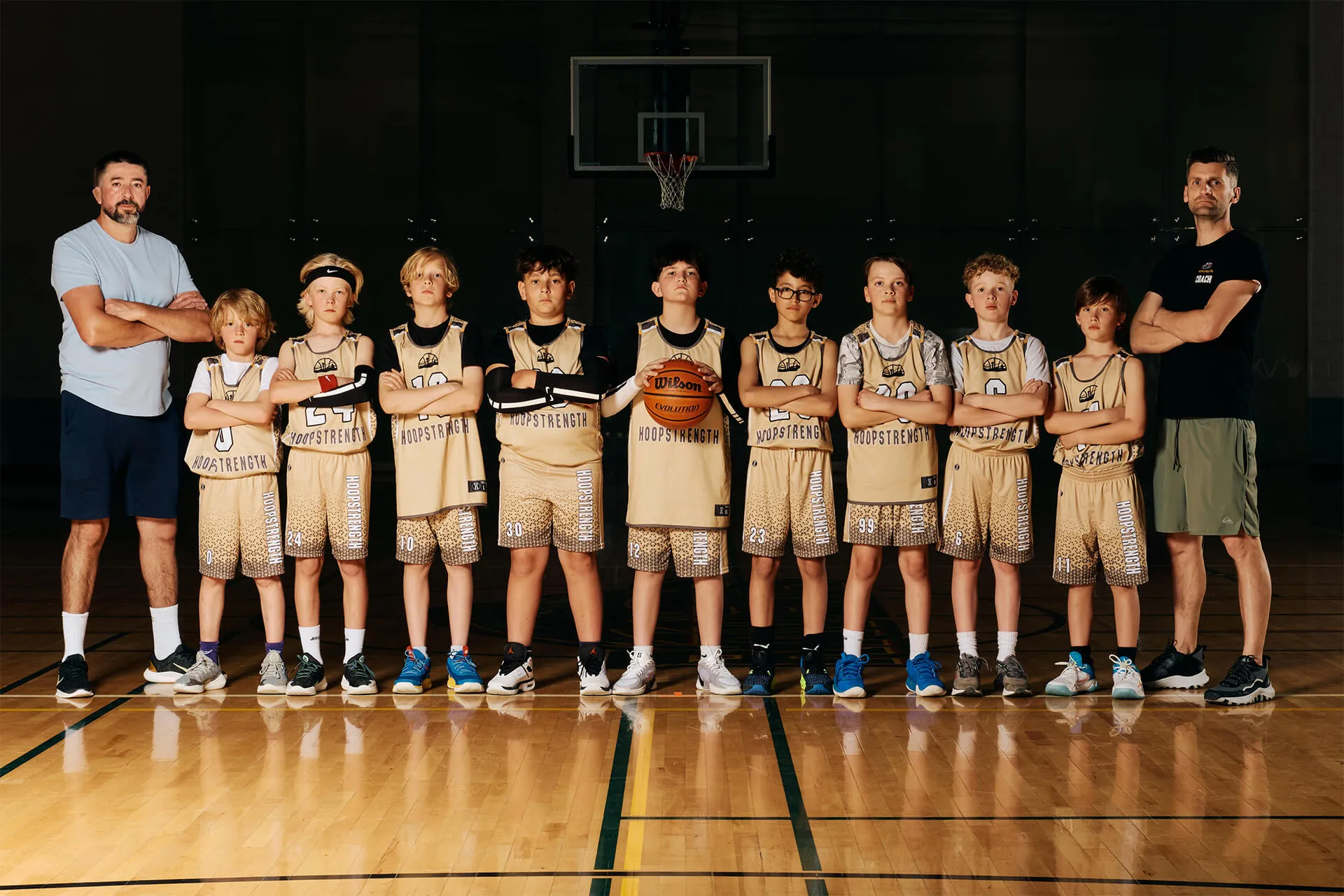 Youth basketball team in gold uniforms standing on a court with arms crossed, flanked by two adult coaches.