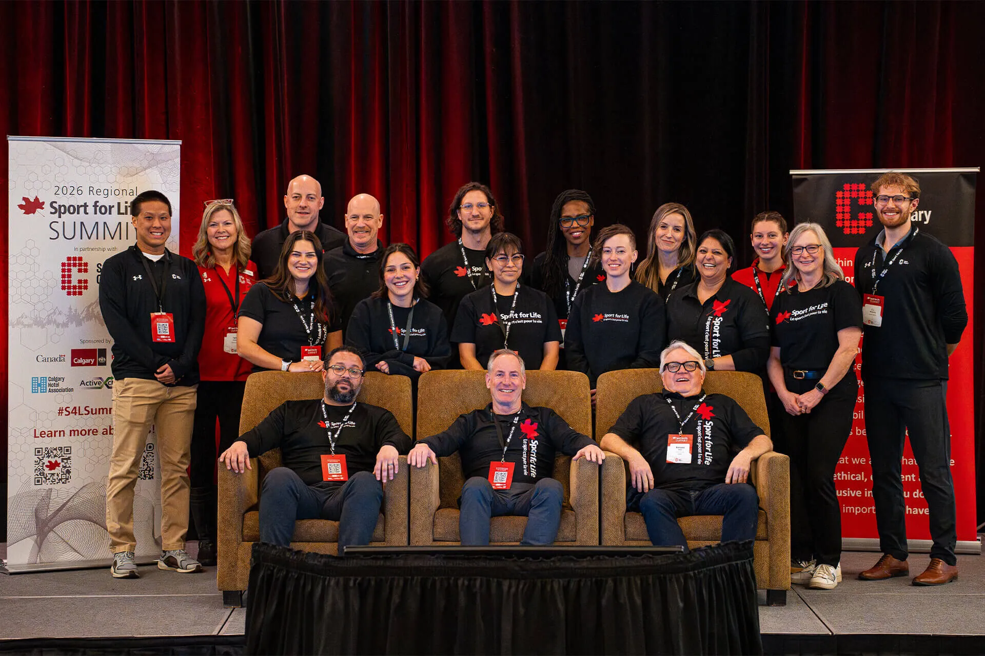 Group of people posing on stage at the 2026 Regional Sport for Life Summit with three men seated in front and others standing behind.