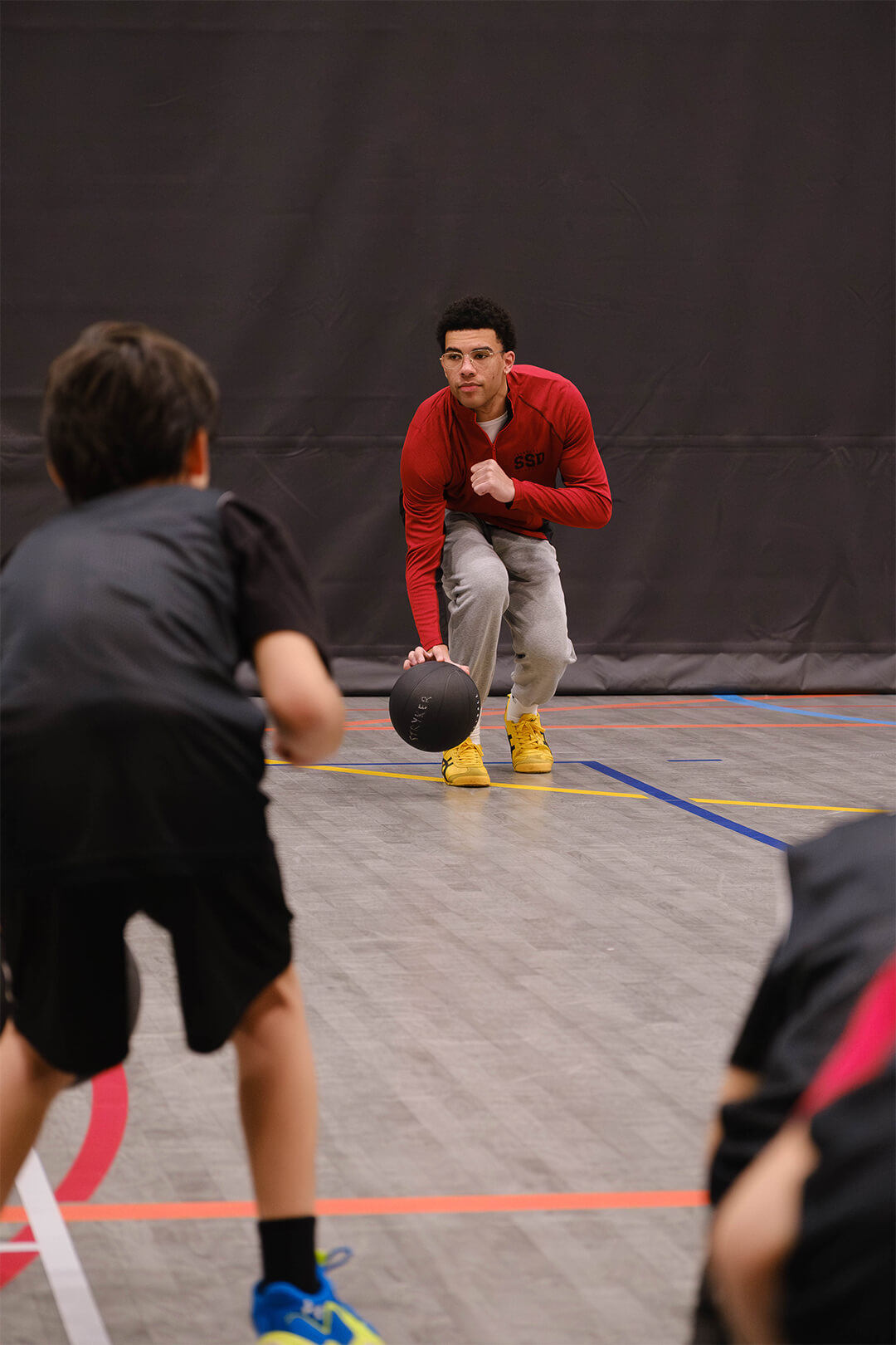 Basketball coach demonstrating ball-handling drill to youth athletes in development program.