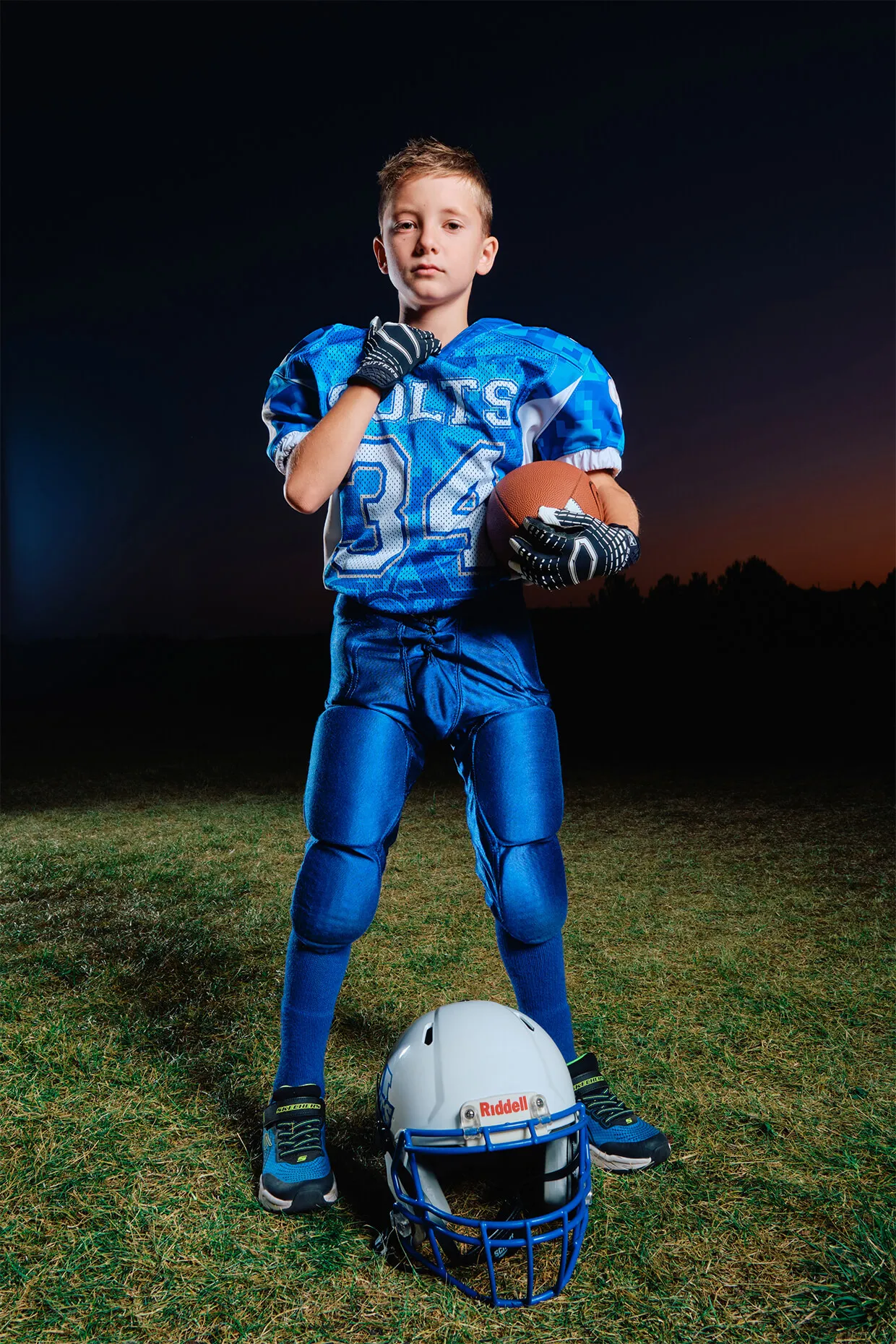 Full-length youth football portrait with helmet on grass during outdoor Media Day production.