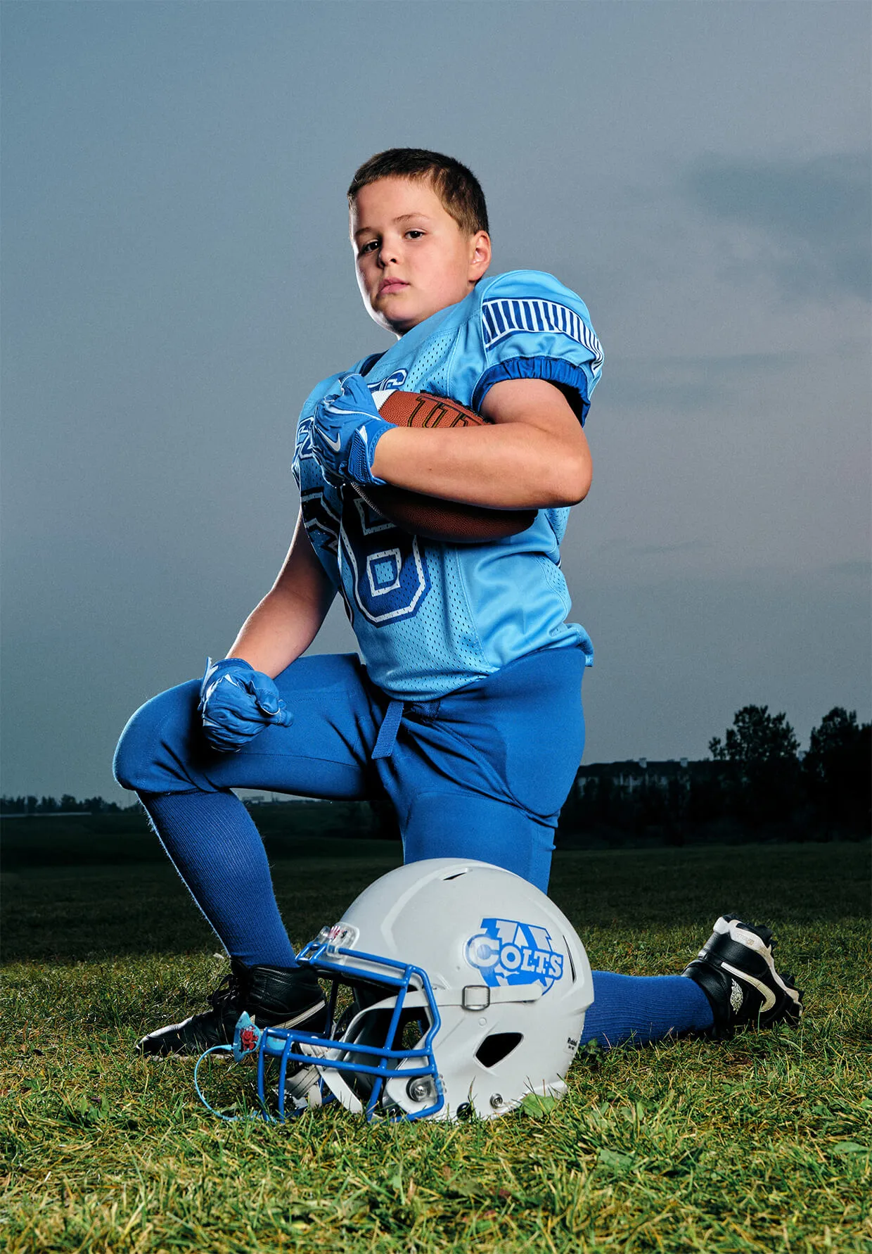 Youth football athlete kneeling with helmet on field during professional team Media Day.