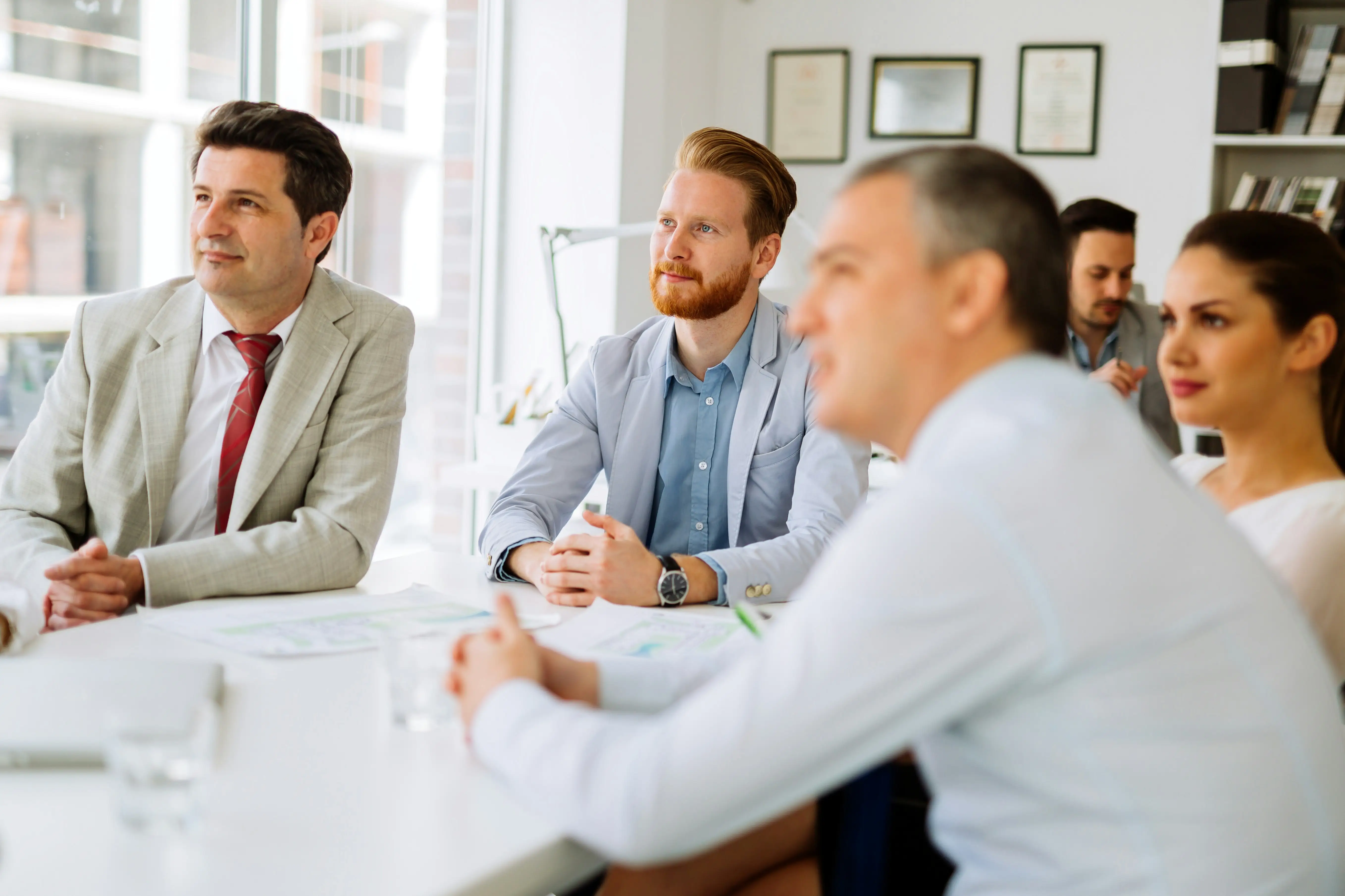 Team sitzt am Meetingisch und schaut aufmerksam nach vorne zur Führungskraft