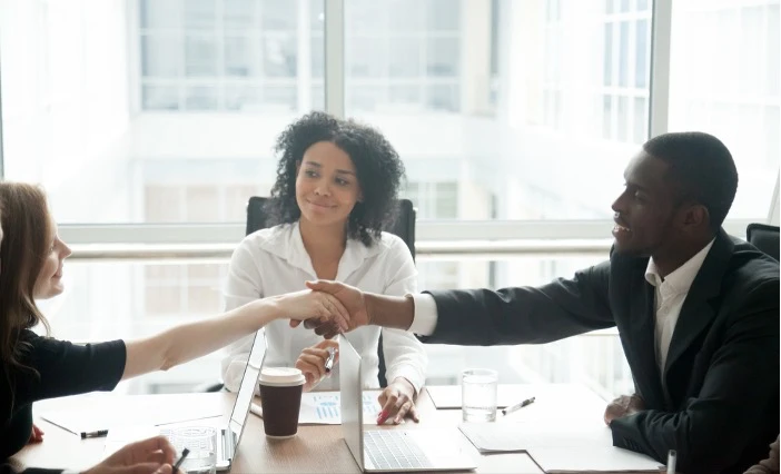 Zwei Mitarbeiter schütteln sich vor ihrer Führungskraft versöhnlich die Hände