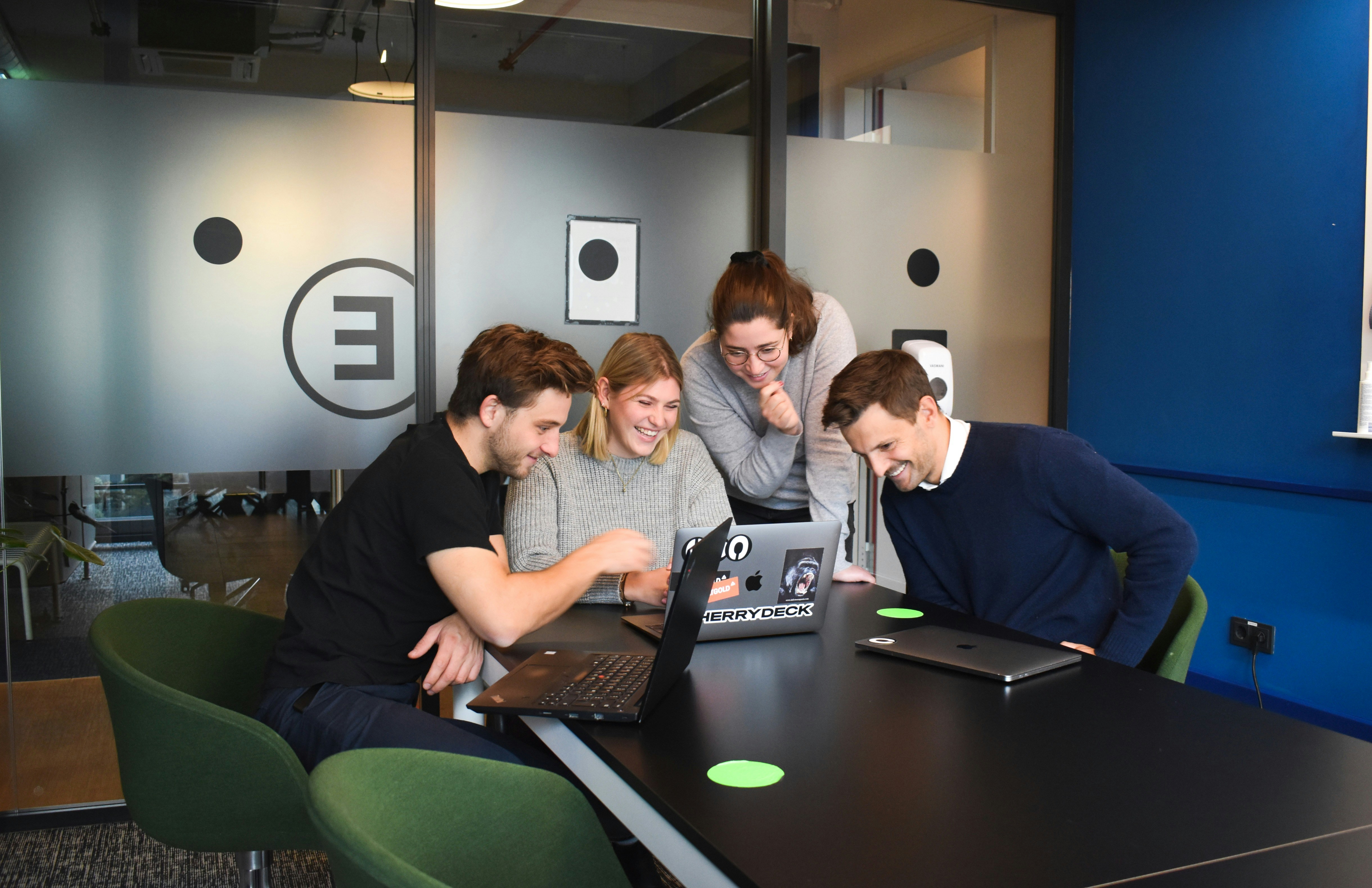 Team schaut gemeinsam lachend auf einen Laptop-Bildschirm im Büro