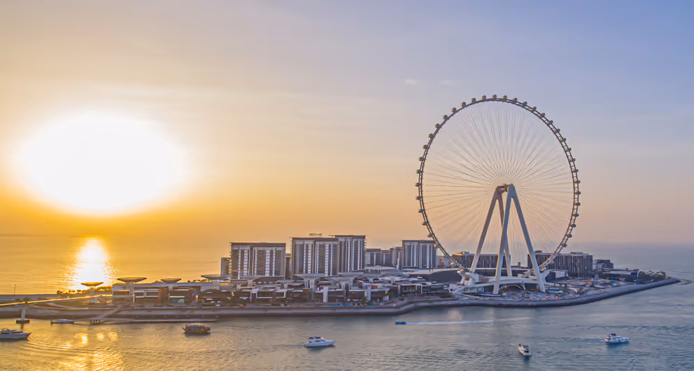 Serene view of Bluewaters Island in Dubai during sunset, featuring the Ain Dubai observation wheel and calm waters with small boats.