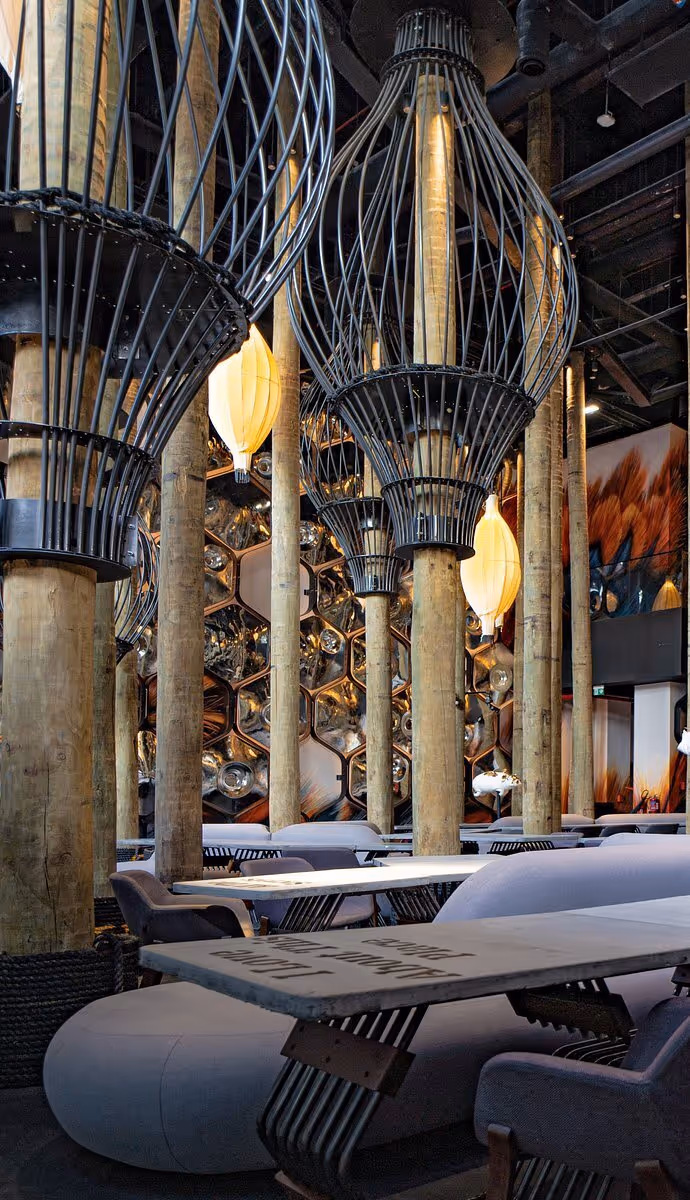 Luxurious interior with ornate golden columns, large hanging lanterns, and plush seating in an opulent lounge or restaurant setting.