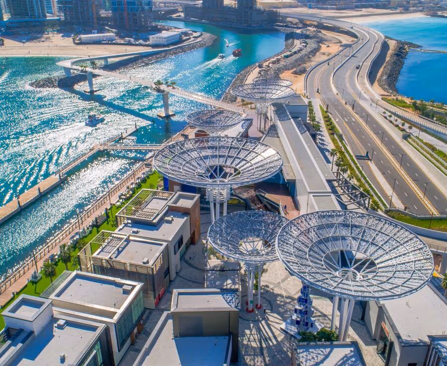 Aerial view of Bluewaters Island in Dubai, featuring futuristic tree-like structures, modern buildings, and nearby highways along the turquoise waterfront.
