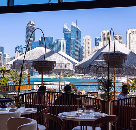 Elegant outdoor restaurant seating at Bluewaters overlooking the water and Dubai Marina skyline with shaded parasols.