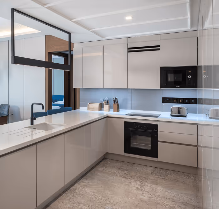 Sleek white kitchen with glossy cabinets, built-in appliances, and a marble floor in a Bluewaters apartment.