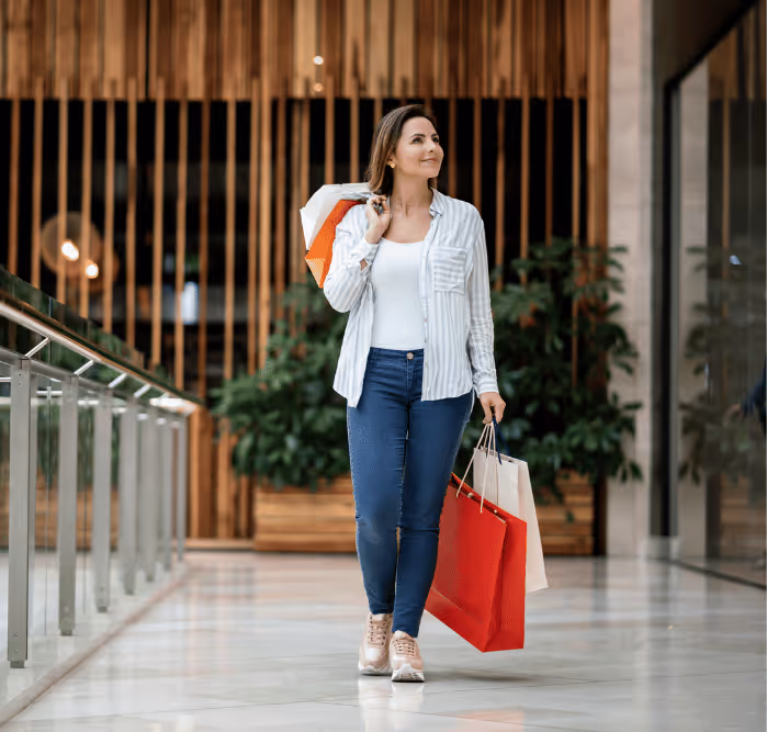 Smiling woman carrying multiple shopping bags while walking through a stylish indoor mall at Bluewaters.