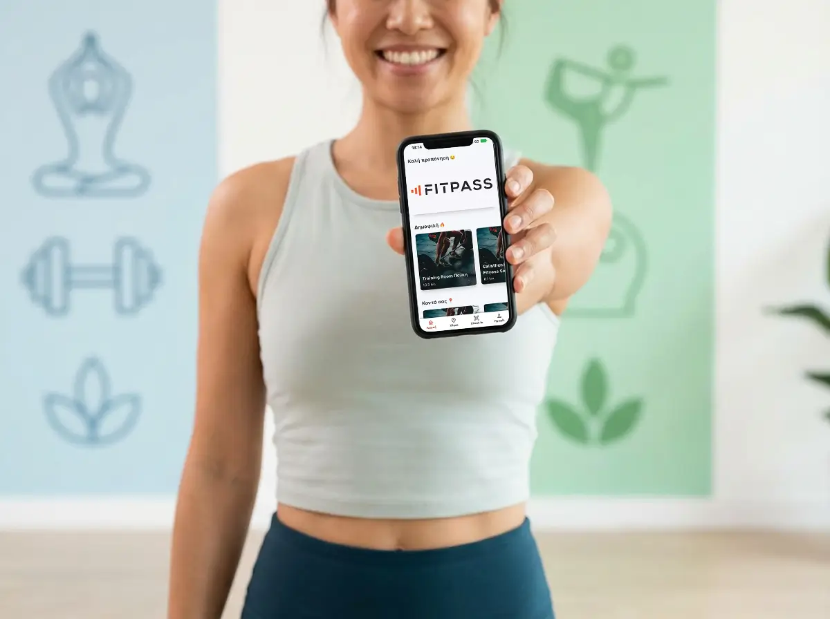 Γυναίκα με αθλητικό τοπ δείχνει μια εφαρμογή fitness FITPASS σε κινητό τηλέφωνο.